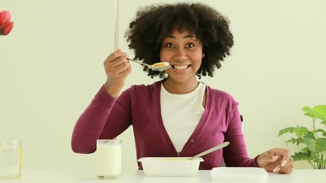 Portrait of an African-American teenage girl eating rice and fried eggs in a plastic container bought at a supermarket with a scoop of rice, shows how happy she is.