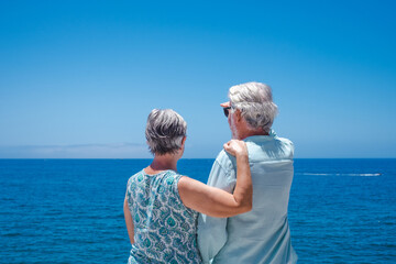 Rear view of caucasian senior couple during vacation standing at the beach looking away enjoying...