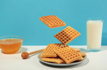 Belgian waffles flying in air on blue and white background. Waffles in plate with milk and honey. Creative food concept.