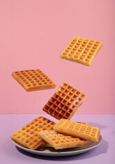 Belgian waffles flying in air on a pasel pink background. Waffles in plate. Creative food concept.