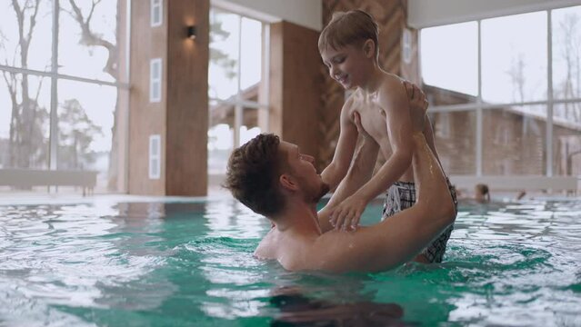happy people in modern wellness center, father and little son are swimming in pool, family weekend in health care complex