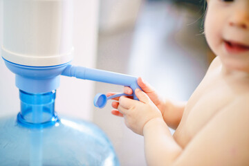 Baby and pump with drinking water. The child learns to pour water. Little cute girl is trying to put pressure on the pump