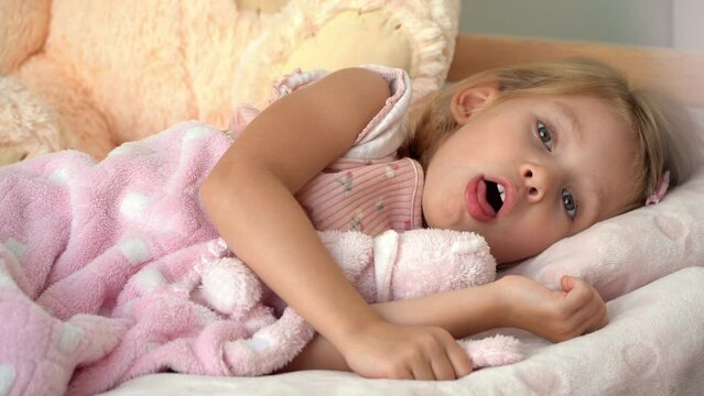 Fathers hands measure sick little daughter temperature with thermometer. Child lies in bed with cough and fever. Treatment for flu and cold