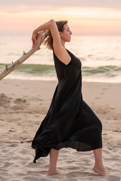 Woman in a black dress with a wooden snag on the seashore, in profile