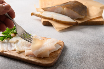 Fototapeta na wymiar Smoked halibut slices on gray background. Man eating delicacy fish. Close up.