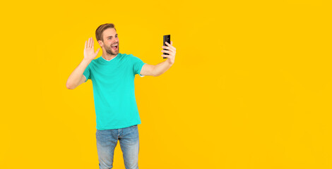 happy unshaven young man making selfie on phone on yellow background, communication