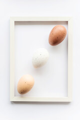 Three natural eco eggs on a white background with copy space for text in a frame. Geometry. Minimal concept. View from above. Easter card, soft selective focus.