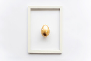 Golden egg with polka dots on a white background with copy space for text in a frame. Minimal concept. View from above. Easter card, soft selective focus.