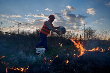 Firefighter ecologist fighting wildfire in field with evening sky on background. Male...