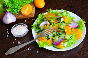 mixed salad with yellow tomatoes, salad leaves and red onion with fork on plate, close-up