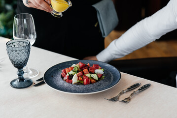 A waiter pours sauce over a fresh salad of vegetables and tuna in close-up. Healthy food. Exquisite...