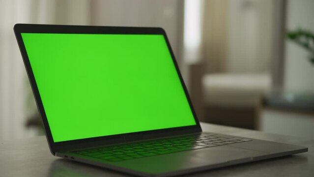 Slow optical zoom out from a laptop with a green screen in apartment