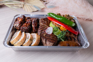 Delivery of healthy restaurant food in a foil box. Grilled meat steak and vegetables. Takeaway food