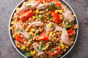 Fresh salad prepared with spelt, tuna, corn, tomatoes and herbs close-up in a plate on the table. horizontal top view from above
