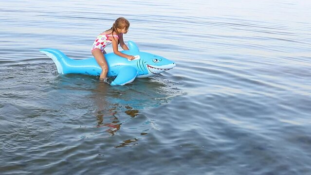  Happy girl swimming on an inflatable shark toy in the sea