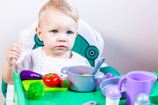 Blurred little child holding a toy vegetable in his hands on the background of dishes