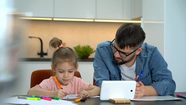 Father and little daughter learn to draw watching drawing lesson on tablet on internet at home. Online education concept. Video tutorial, drawing training.