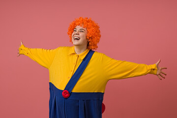 cheerful clown, joyful girl in a wig spread her arms to the sides on a colored background