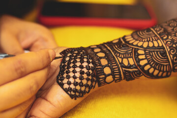 An artist performing mehandi or henna design on female hand.