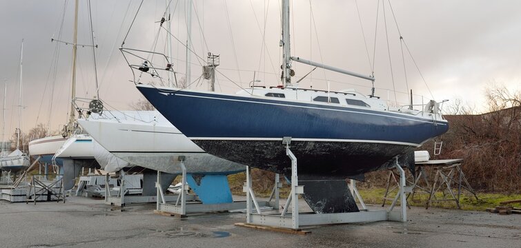 Blue sloop rigged sailboat standing on land in a yacht club. Service, repair, transportation, sport, recreation, leisure activity