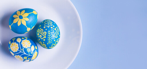 Macro view of Easter eggs on white plate painted with Ukrainian national colors, blue and yellow, and depicting Ukrainian ornaments