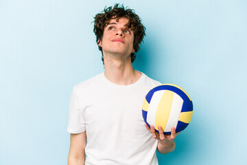 Young caucasian man playing volleyball isolated on blue background dreaming of achieving goals and purposes