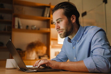 Young bristle man working with laptop while sitting at desk