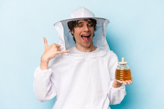 Young caucasian beekeeper man isolated on blue background showing a mobile phone call gesture with fingers.