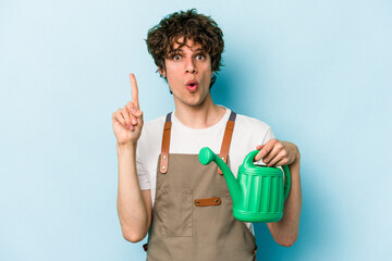 Young gardener caucasian man holding watering can isolated on blue background having some great idea, concept of creativity.