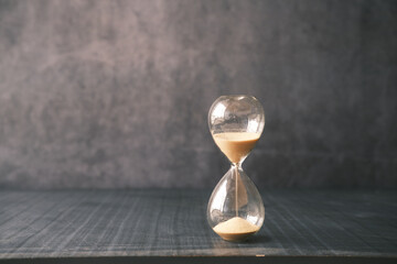hourglass on table, sand flowing through the bulb of sandglass - obrazy, fototapety, plakaty