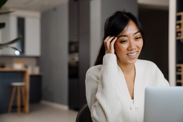 Asian woman with brace laughing while working with laptop
