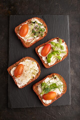 Red beet bread sandwiches with cream cheese, tomatoes and microgreen on black. top view.