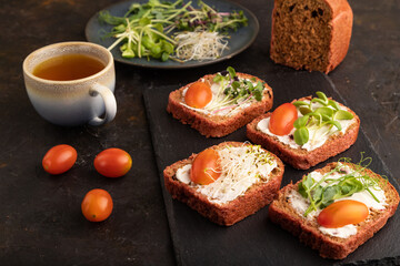 Red beet bread sandwiches with cream cheese, tomatoes and microgreen on black. side view.