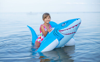  Happy girl swimming on an inflatable shark toy in the sea