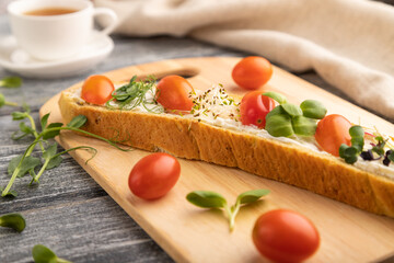 Long white bread sandwich with cream cheese, tomatoes and microgreen on gray. side view, selective focus.