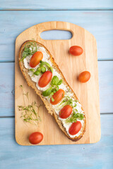 Long white bread sandwich with cream cheese, tomatoes and microgreen on blue. top view.