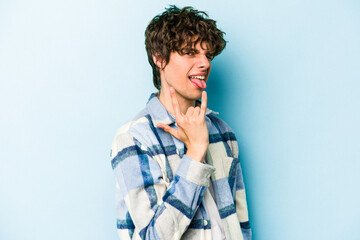 Fototapeta premium Young caucasian man isolated on blue background showing rock gesture with fingers