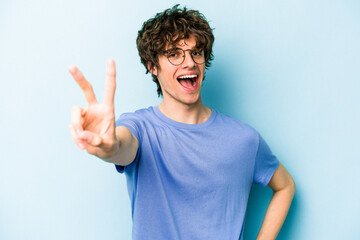 Fototapeta premium Young caucasian man isolated on blue background joyful and carefree showing a peace symbol with fingers.