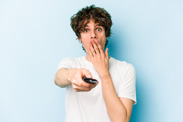 Young caucasian man holding tv controller isolated on blue background