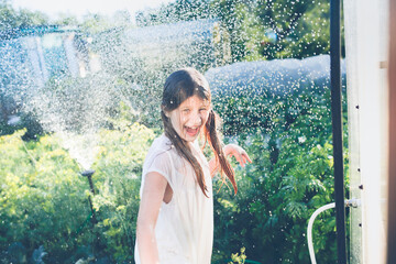 Hot summer and garden. Children bathe under the spray of a garden watering system. Children dance and jump under the spray of the garden fountain
