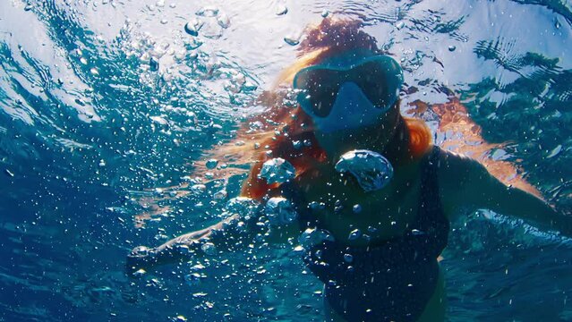 Woman in white mask swimming and snorkeling in the tropical sea in Maldives with a lot of bubbles