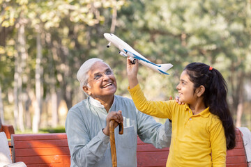Senior man with granddaughter having fun flying toy airplane at park