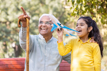 Fototapeta premium Senior man with granddaughter having fun flying toy airplane at park