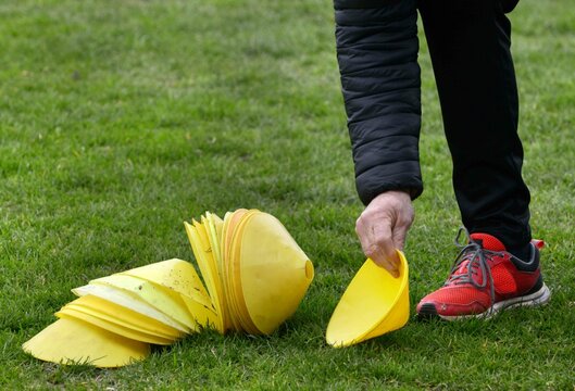 l'assistant ramasse les cônes d'entrainement sur le terrain au football	