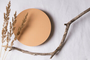 Empty round beige platform podium, dry tree twigs and bent grass on white linen fabric background. Minimal creative composition background for cosmetics or products presentation. Top view
