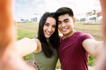 Multiethnic young couple taking selfie together outdoors during vacation - Asian man enjoying summer holidays with his girlfriend