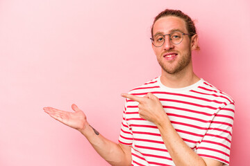 Young caucasian man isolated on pink background excited holding a copy space on palm.