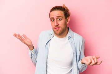 Young caucasian man isolated on pink background doubting and shrugging shoulders in questioning...