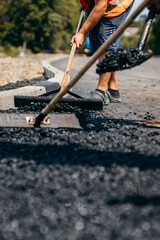 Road workers with shovels in their hands throw forked asphalt on a new road. Road service repairs the highway