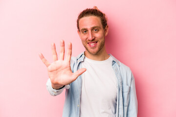 Young caucasian man isolated on pink background smiling cheerful showing number five with fingers.
